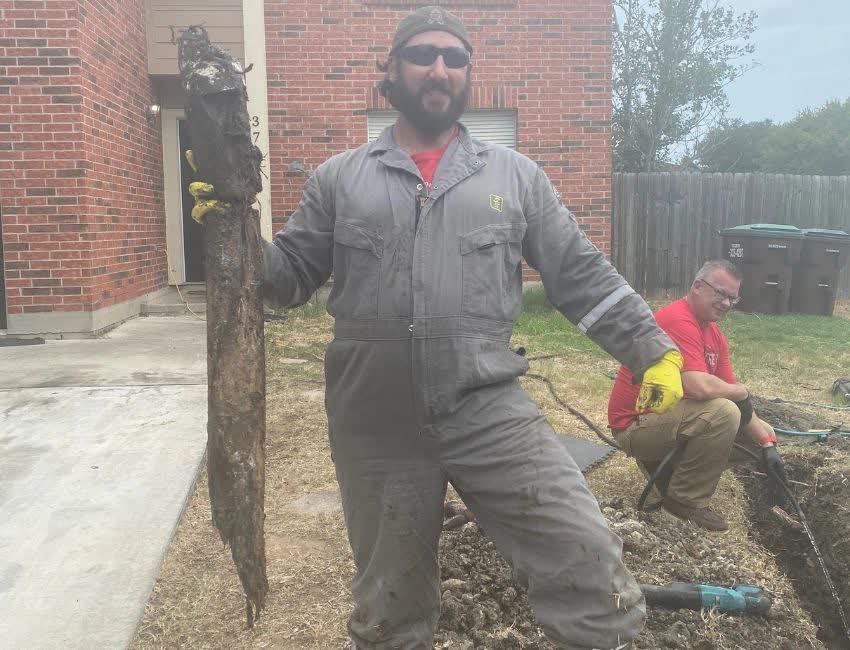 5th Street Services tech holding a failed sewer pipe pulled from under a home