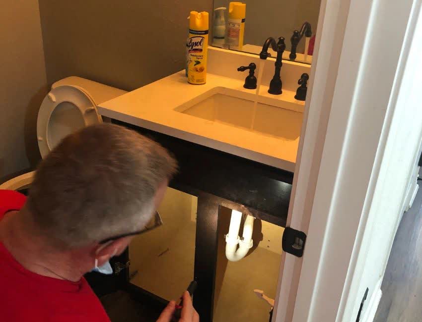 Technician repairing plumbing under a bathroom sink